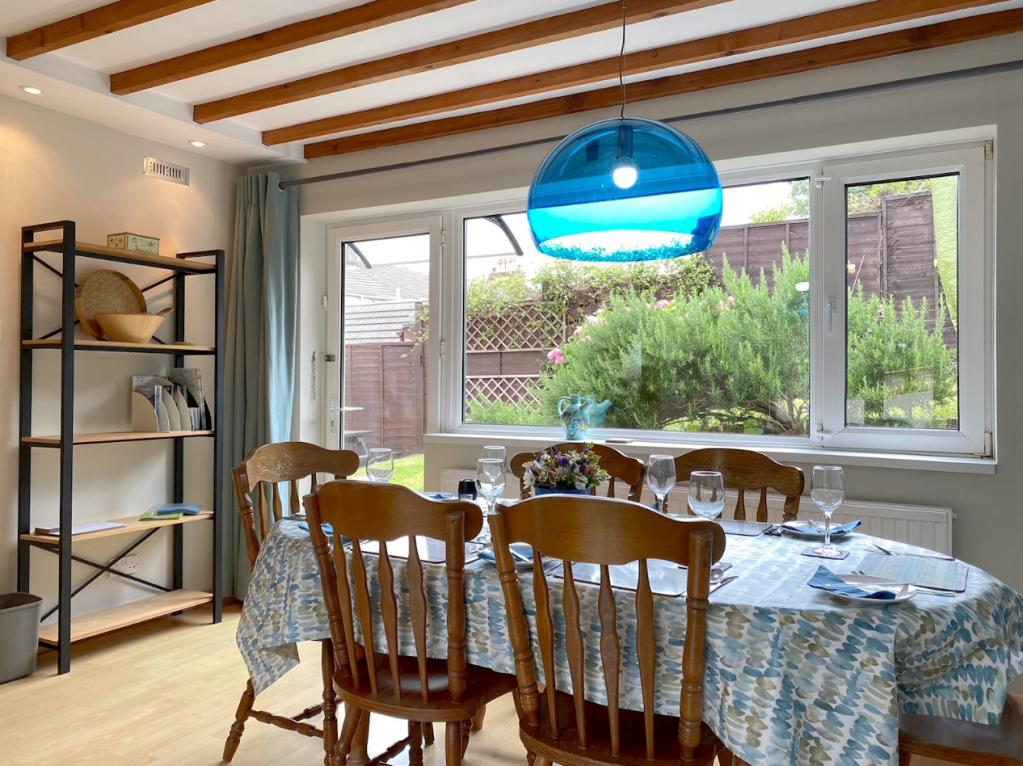 The dining room at The Little Red House Mumbles holiday cottage, with 6-seater table and doors to two terrace areas with seating.